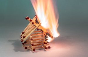 A little house built of matchsticks, with the matchsticks on fire