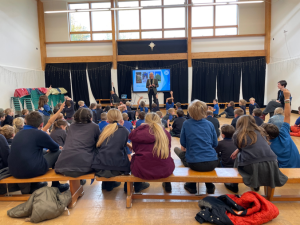 Shows the clerk and the chair of Moretonhampstead Parish Council visiting the local school and talking to children in an assembly.